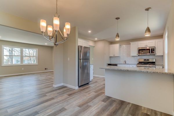Open-concept kitchen and living room with white cabinets, stainless steel appliances, and wood-look flooring.