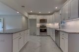 Bright white kitchen with stainless steel appliances, white cabinets, and gray countertops.