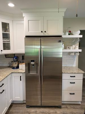 Stainless steel refrigerator in a white kitchen with upper cabinets.