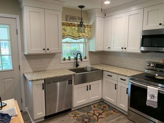 White kitchen cabinets, stainless steel appliances, granite countertops, farmhouse sink, and a colorful rug.