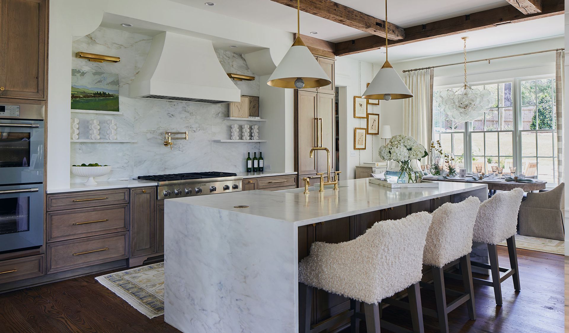 Elegant kitchen with white cabinets, marble backsplash, island with seating, and gold accents.