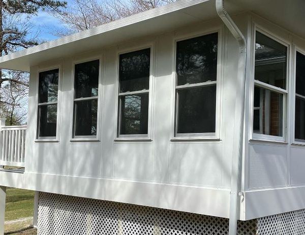 White sunroom with multiple rectangular windows; latticework base, white railing.