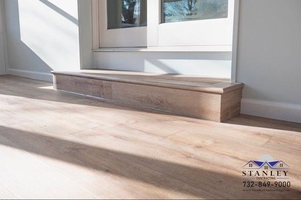 Wooden step in front of a window, built-in to the light wood flooring.