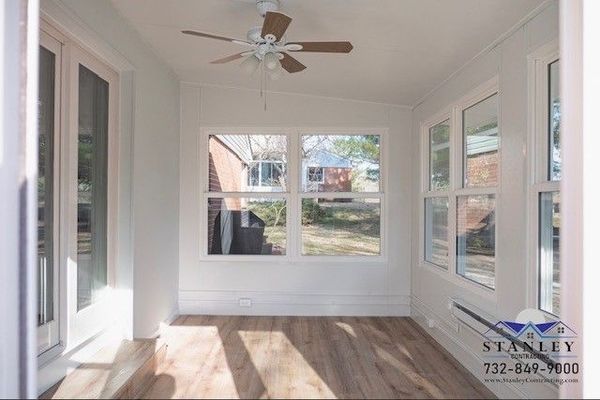 Sunroom interior with windows, wood floor, ceiling fan, and white walls.