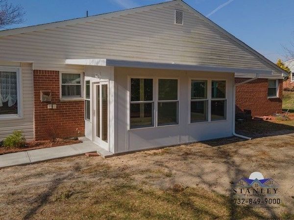 White sunroom addition with glass windows and door, attached to a brick house with a concrete walkway.