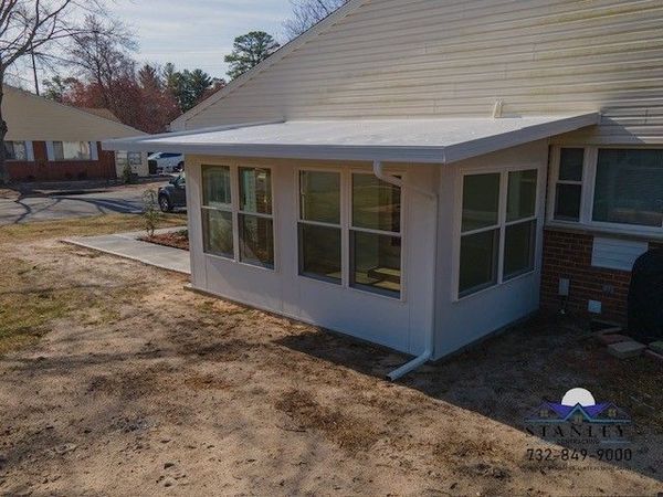 White sunroom addition with windows and a sloped roof, attached to a house.