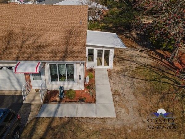 Brown-roofed house with white trim, awning, and attached add-on. Concrete walkway leads to the entrance.