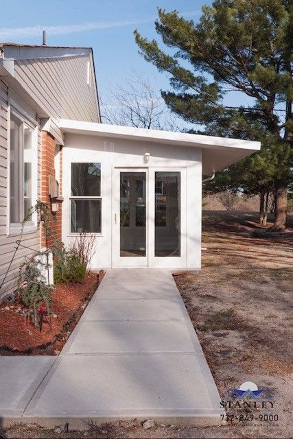 A concrete path leads to a white enclosed entrance with glass doors and windows, next to a building.