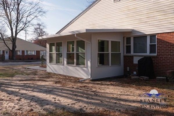 A white sunroom addition to a brick building. The room has large windows and a tan roof.