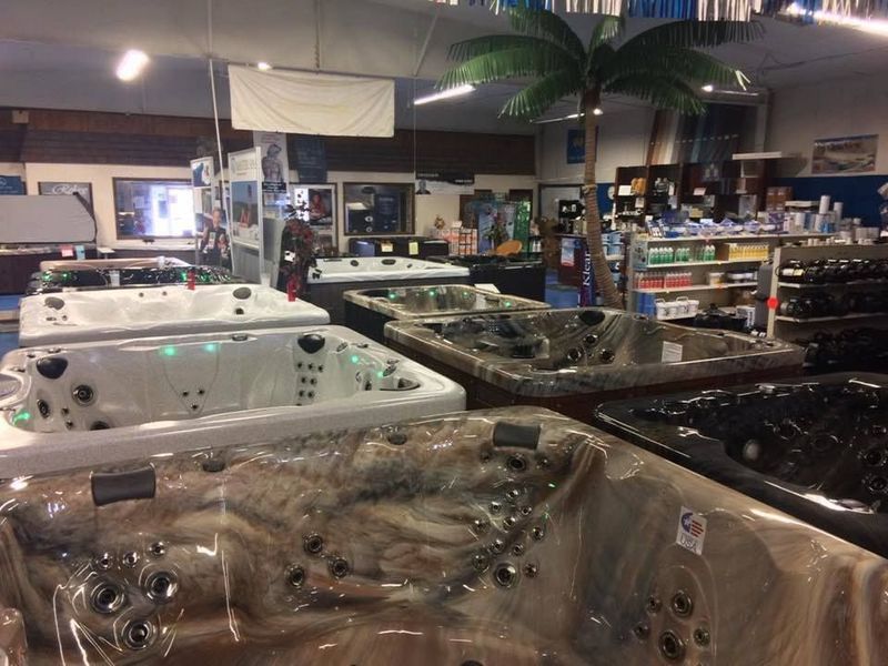 Indoor showroom with multiple hot tubs on display. Palm tree decor.