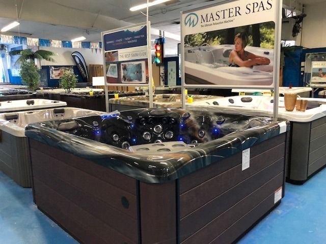 Hot tub display in a store. Brown and black spas with Master Spas signage; blue lights, wood-like paneling.