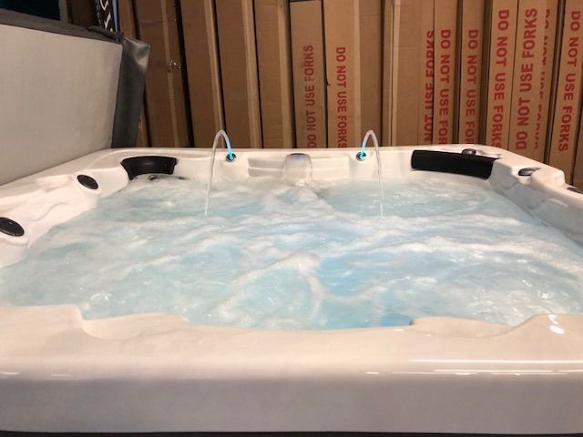 A bubbling, white hot tub with water fountains, boxes in background.