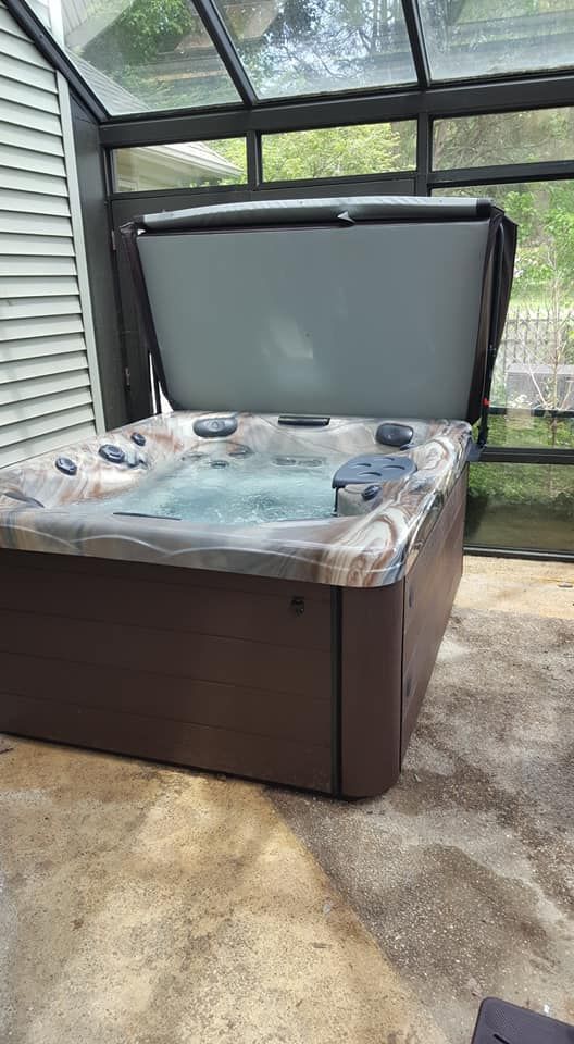 Hot tub with open gray cover in a sunroom with glass panels.