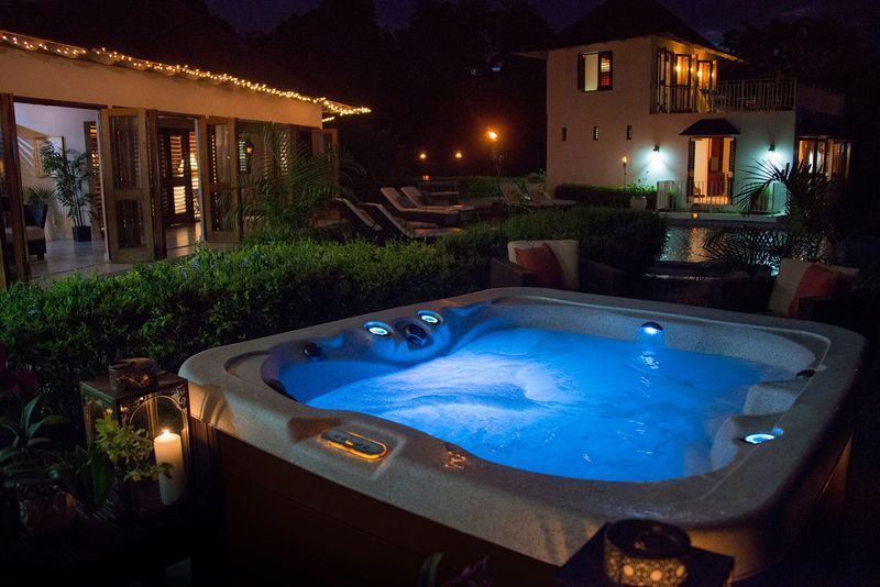 Lit hot tub at night, outdoor setting with lights. Two-story building and wooden structures in background.