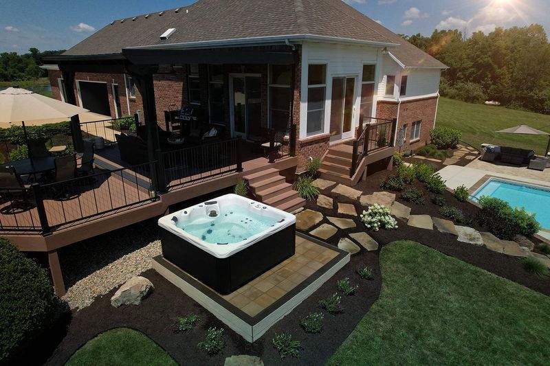 Hot tub in a backyard with deck, pool, and landscaped yard under a sunny sky.
