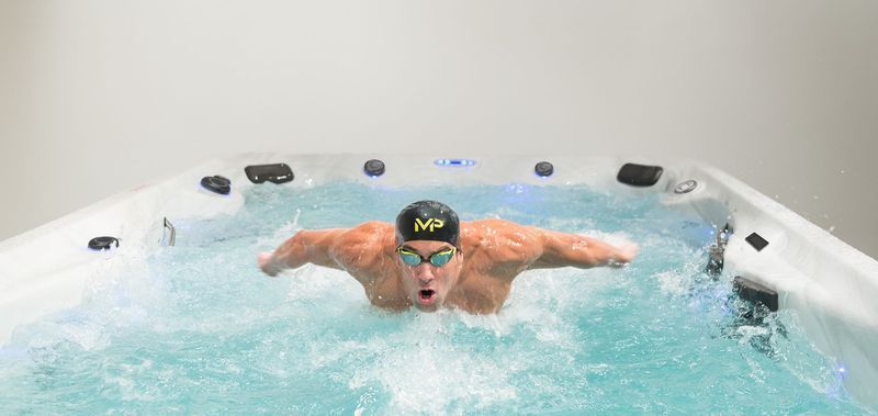 Swimmer in goggles and cap doing the butterfly stroke in a small, white swim spa.