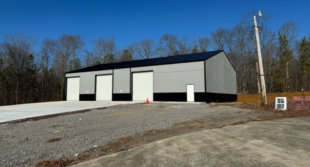 A large building is sitting on top of a gravel lot in the middle of a forest.
