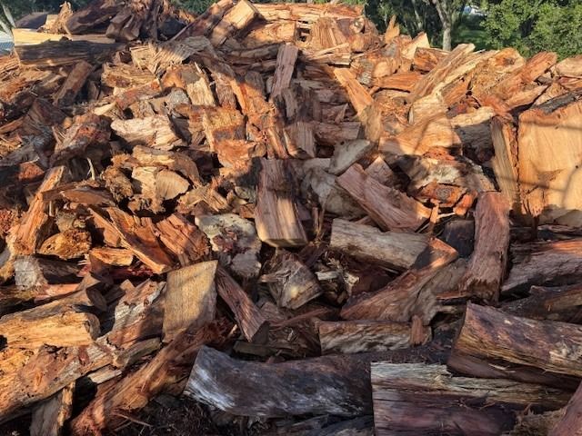 Pile of split firewood, various shapes and sizes, mostly brown and reddish hues.