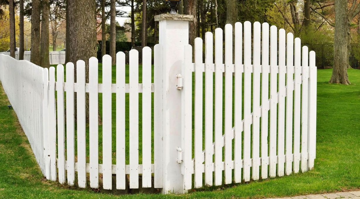 White picket fence with a gate, curving around a grassy lawn.