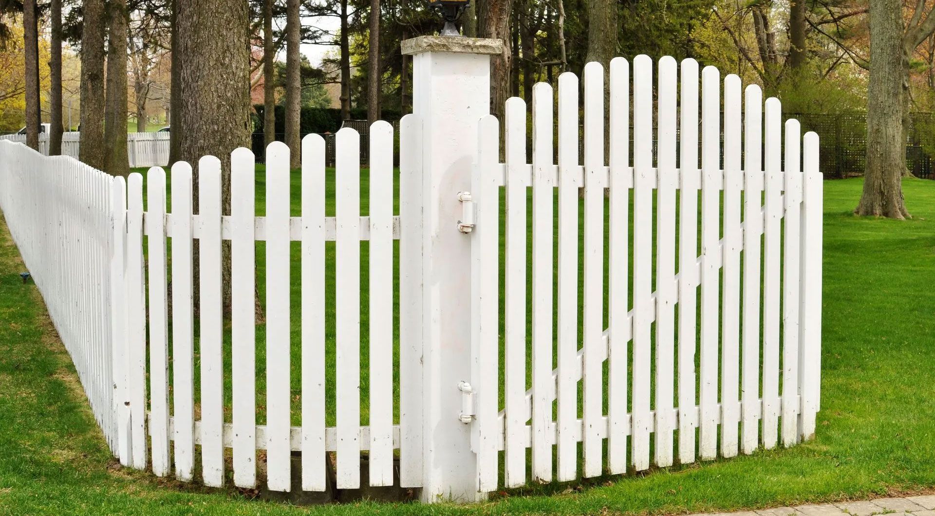 White picket fence with a gate, curving around a grassy lawn.