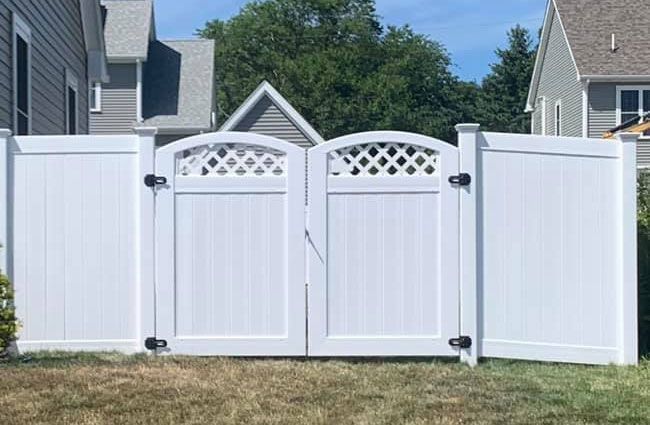 White vinyl double gate in a backyard, with lattice top and black hardware.