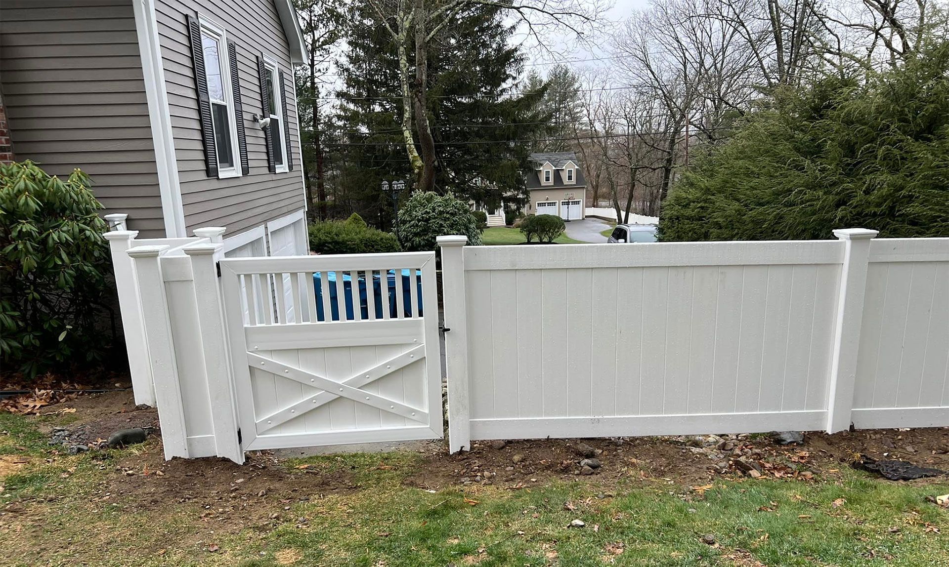 White vinyl fence with gate in front of a house. The gate has an X design.