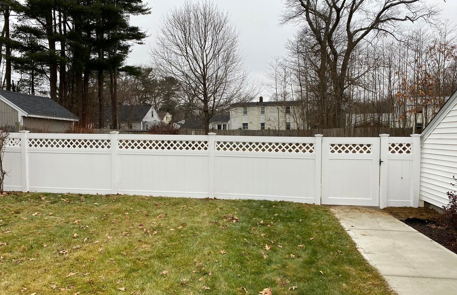 White vinyl fence with lattice top in front yard, with grass and houses in the background on an overcast day.
