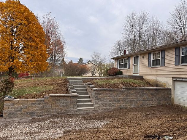 A newly built stone retaining wall with central concrete steps leading up to the lawn of a residential home.
