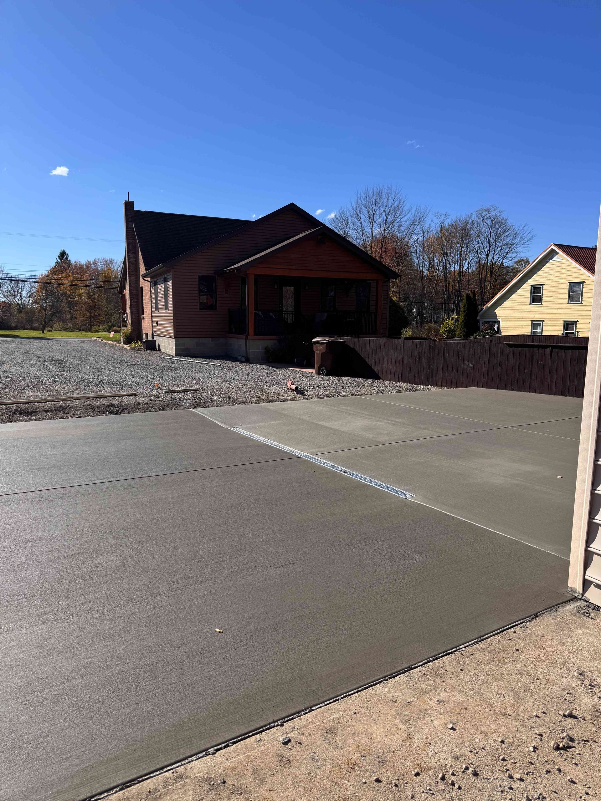 A freshly poured concrete driveway in the foreground leading to a small house under a clear blue sky.