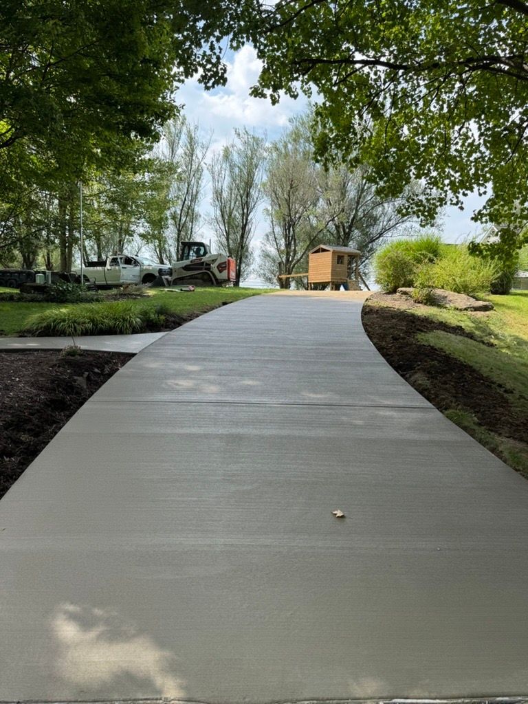 Curved concrete walkway through a leafy park toward a small building on a cloudy day