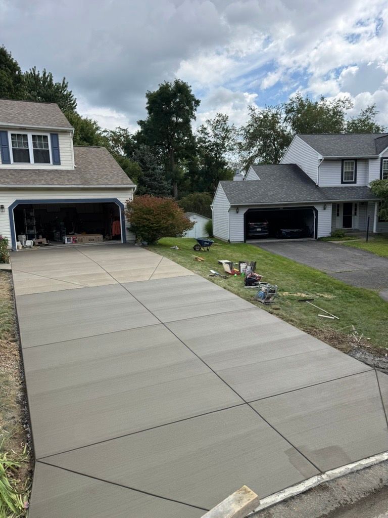 Freshly poured concrete driveway leading to two suburban houses with open garages under a cloudy sky