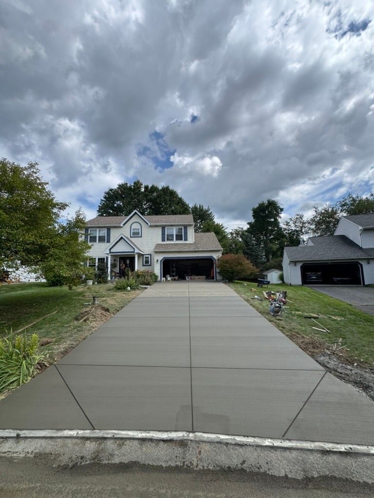 Suburban house with a long concrete driveway under a cloudy sky