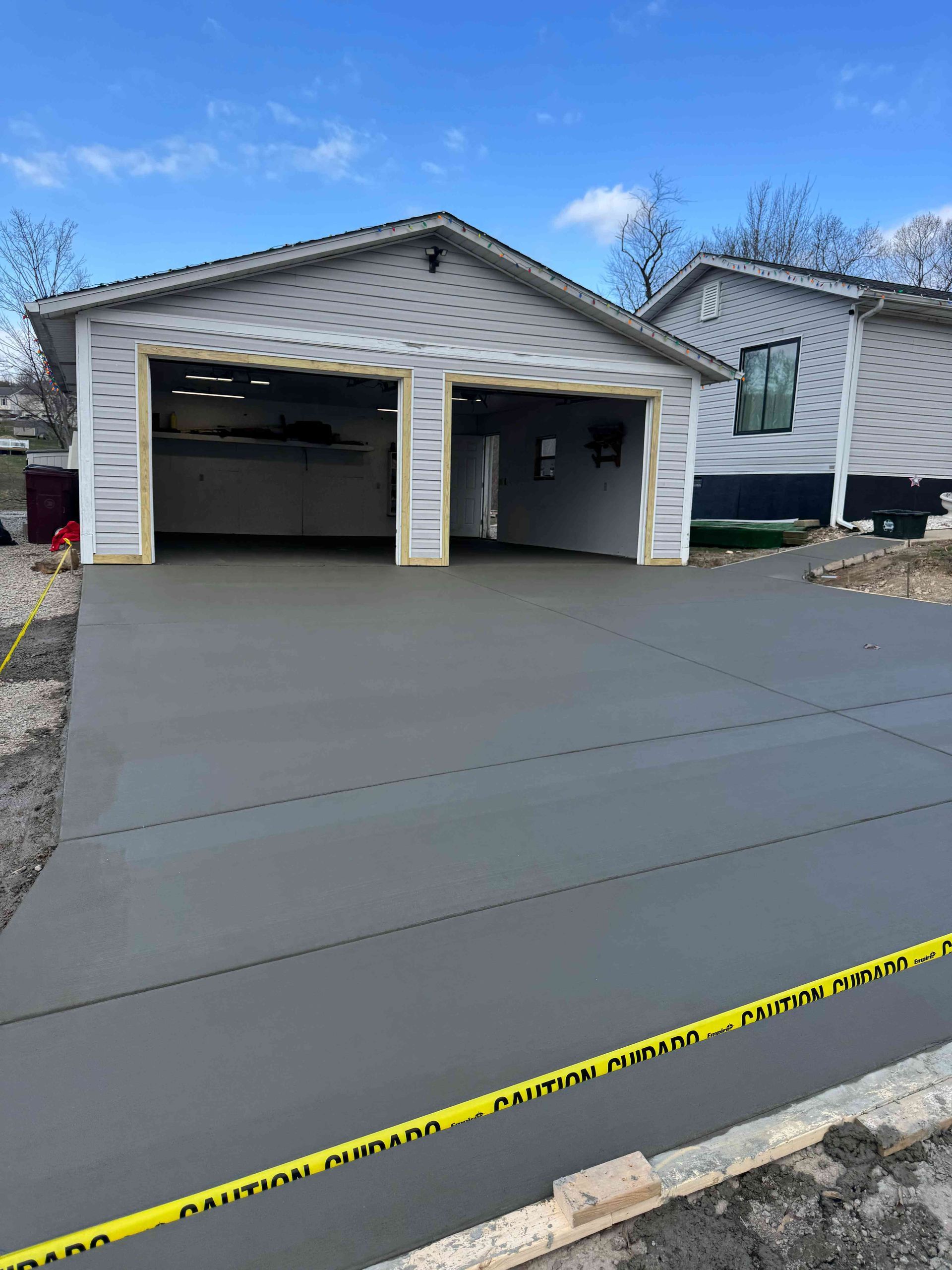 A newly poured gray concrete driveway leads to a garage with unfinished, light-colored siding under a blue sky.