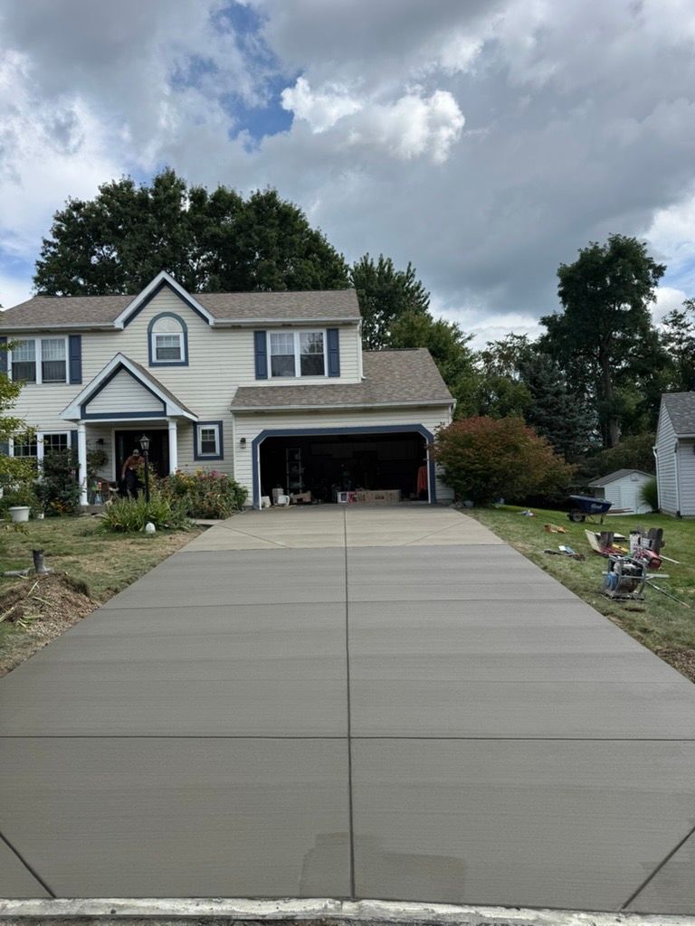 Suburban house with a long concrete driveway and cloudy sky overhead