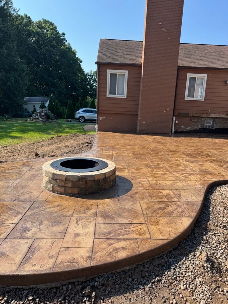 Backyard brick patio with a circular fire pit beside a house and lawn