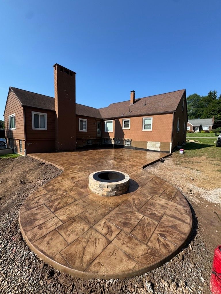 Backyard patio with circular brick fire pit and a brick house under a clear blue sky