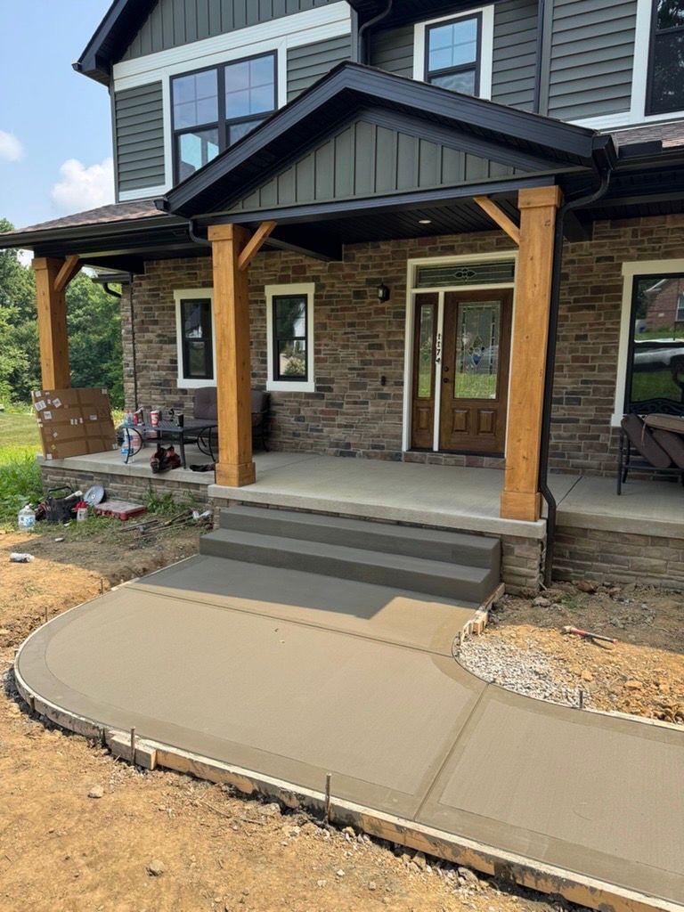 Front porch of a new house with stone steps, wood columns, and a curved concrete walkway.