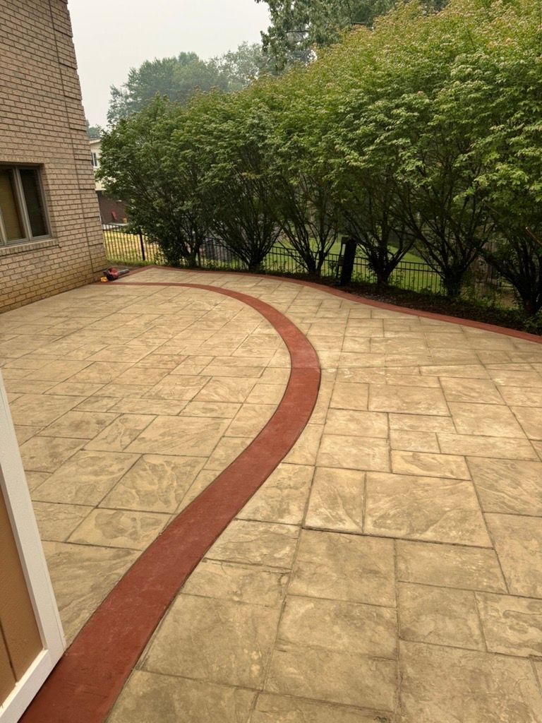 Curved stone walkway beside a brick house and dense green shrubs in a quiet yard