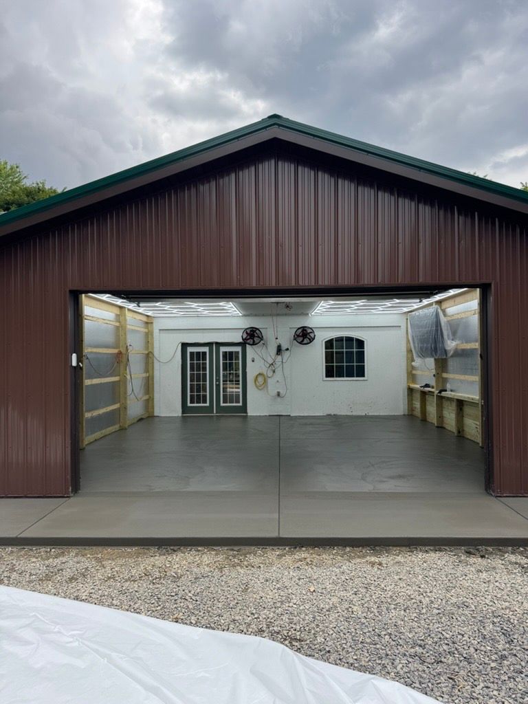 Open garage-style workshop with white interior, shelves on both sides, and gravel driveway outside