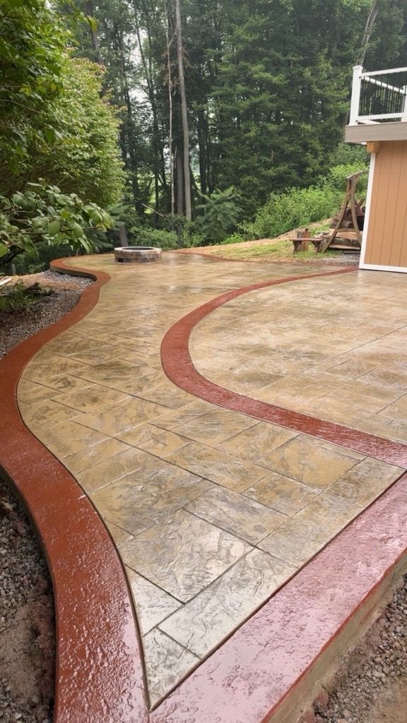 Curved stone patio with red borders beside a wooded backyard and house deck