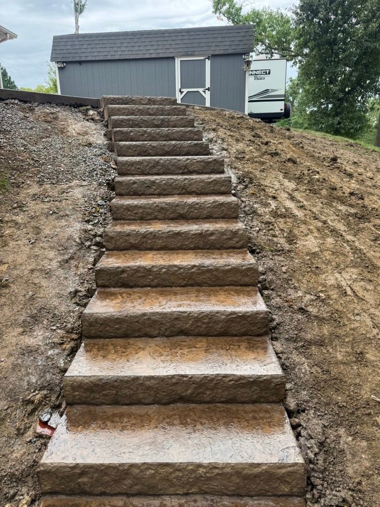 Steep concrete steps up a dirt slope to a gray shed and small building.