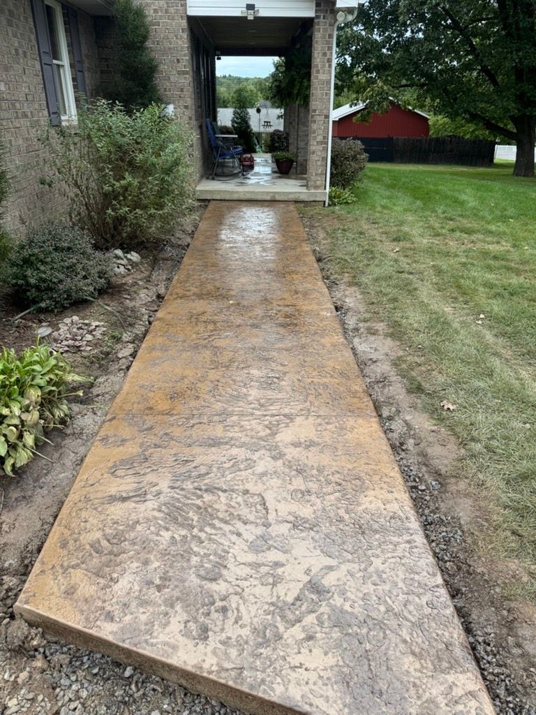Concrete walkway leading to a house entrance, with grass and shrubs on either side