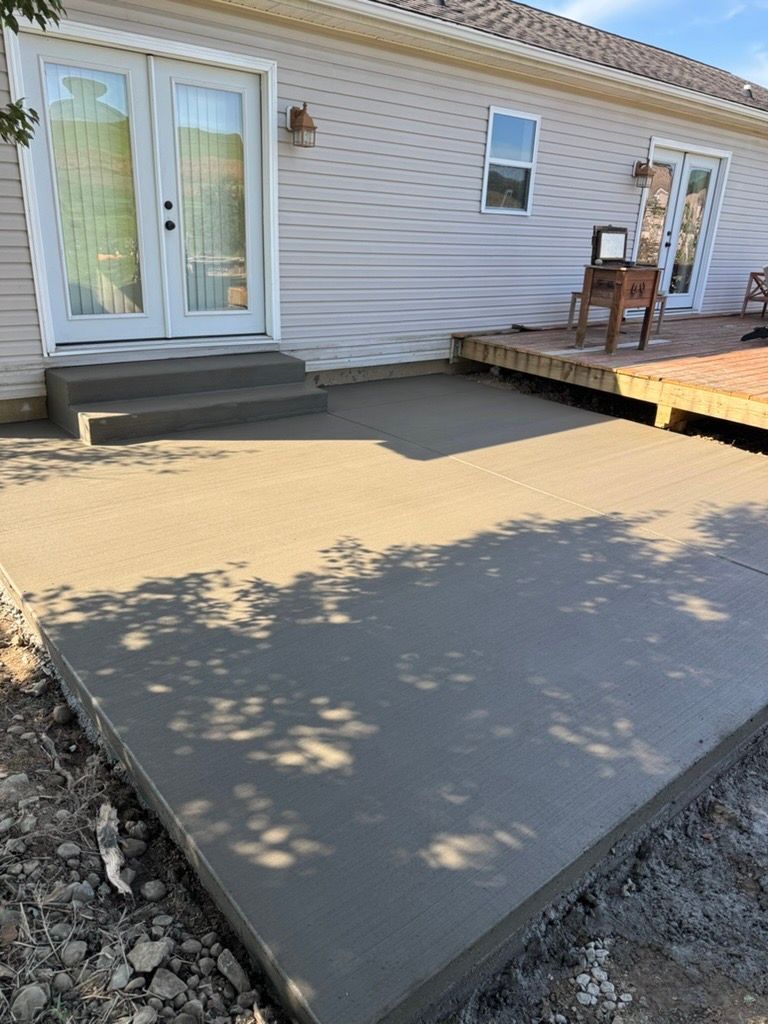 Concrete patio beside a house with sliding glass doors and a small wooden deck with chairs