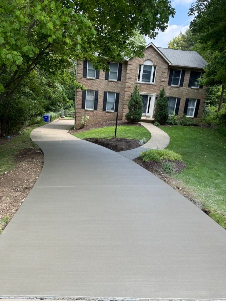 Curved concrete walkway leading to a brick house with a green lawn and trees on either side.