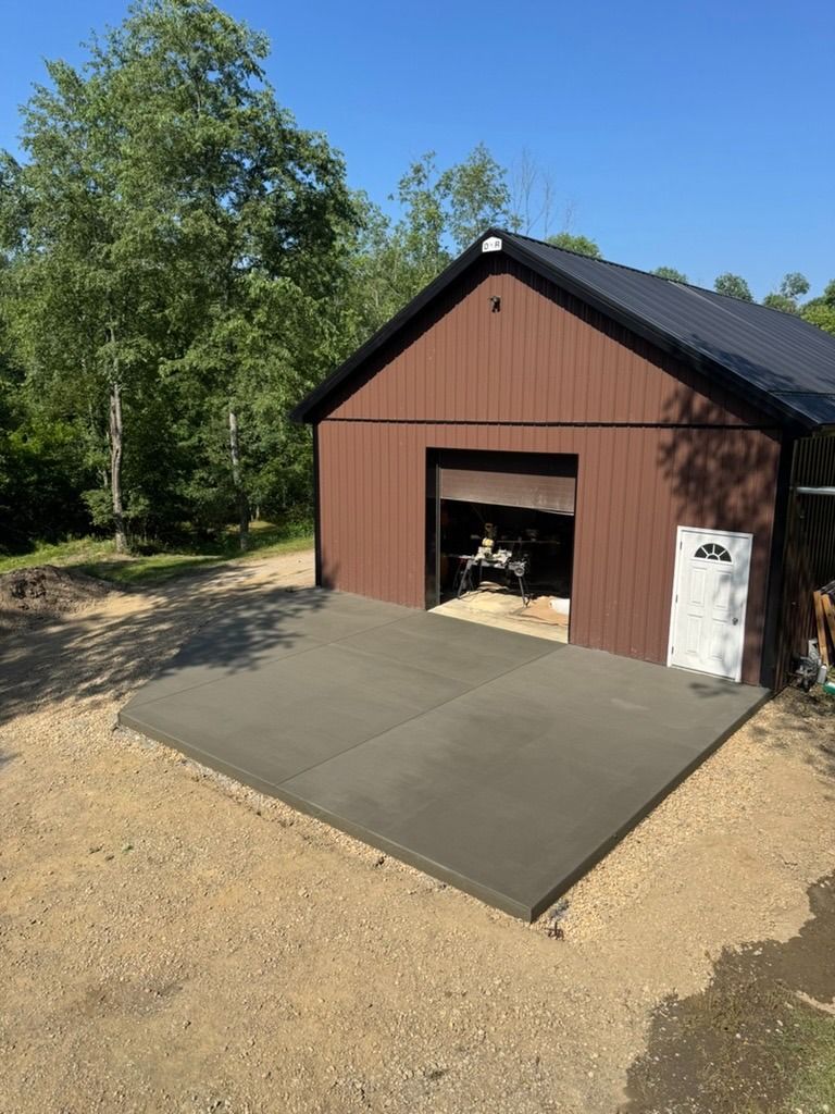Small brown garage with open door, concrete driveway, and trees in the background