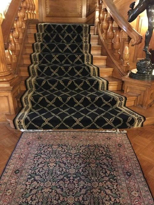 Wooden staircase with a black and gold patterned runner rug, Persian rug at the bottom, and bronze statue.