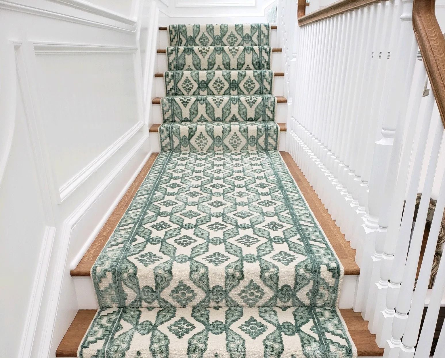 Staircase with patterned teal and cream carpet runner, white risers and banister, wooden steps.