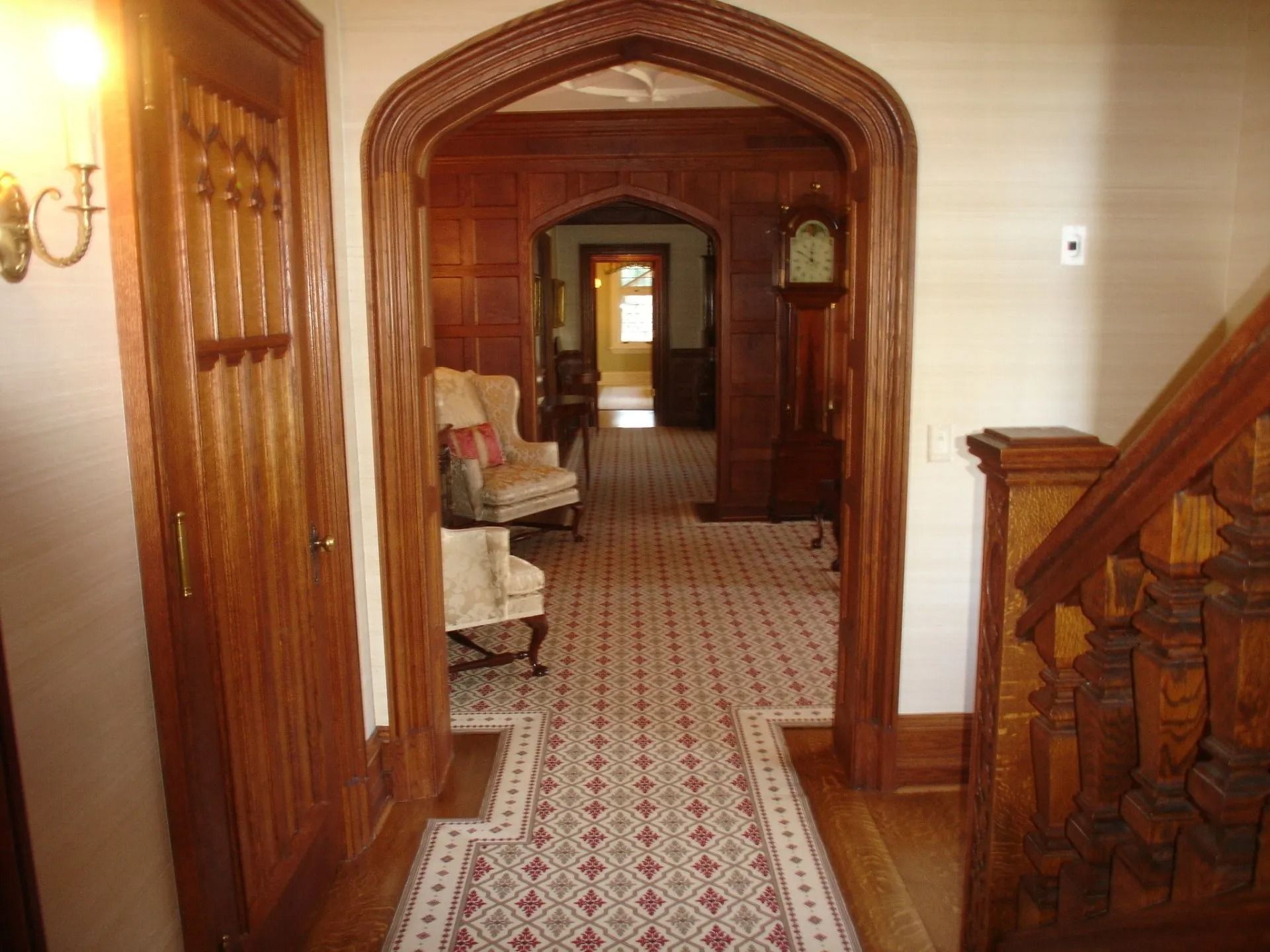 Wood-paneled hallway with arched doorways, patterned tile floor, and a grandfather clock.