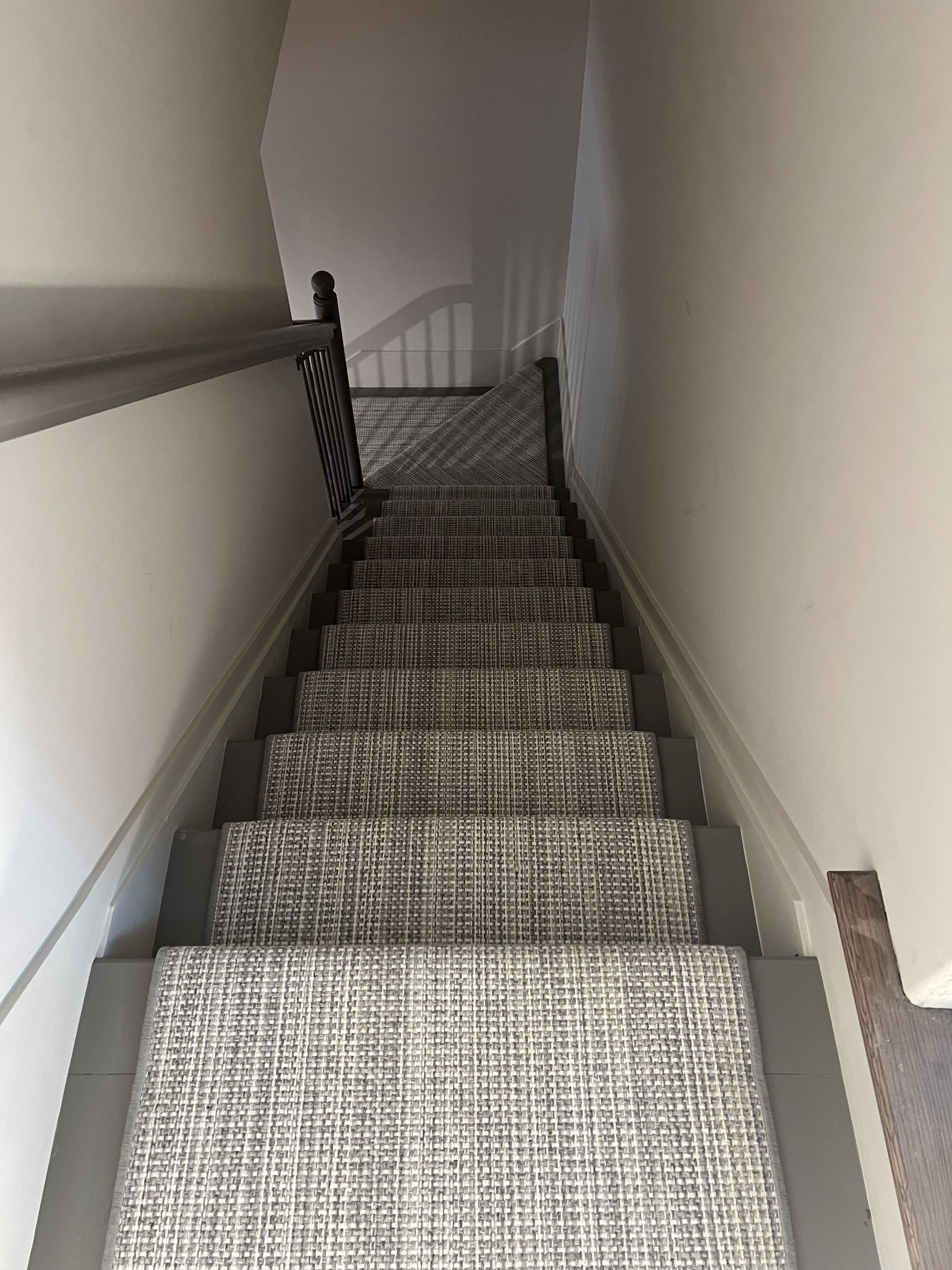 A top-down view of a staircase featuring grey and white patterned carpet treads with dark painted side borders.