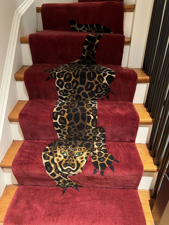 A leopard-print runner decorates a set of stairs carpeted in deep red, with a leopard face featured on the bottom step.